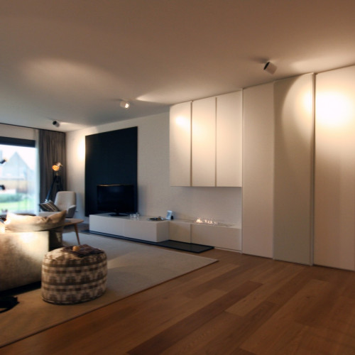 In de woonkamer van dit moderne appartement zorgden we voor een hele kastenwand waarin alle functies van de leefruimte tot uiting komen. In deze lange kastenwand zitten zowel een barkast - die compleet voorzien is van glazen leggers, LED-verlichting en een spiegel als rugwand - servieskast, haardmeubel als TV-meubel. Kast-ID Antwerpen
